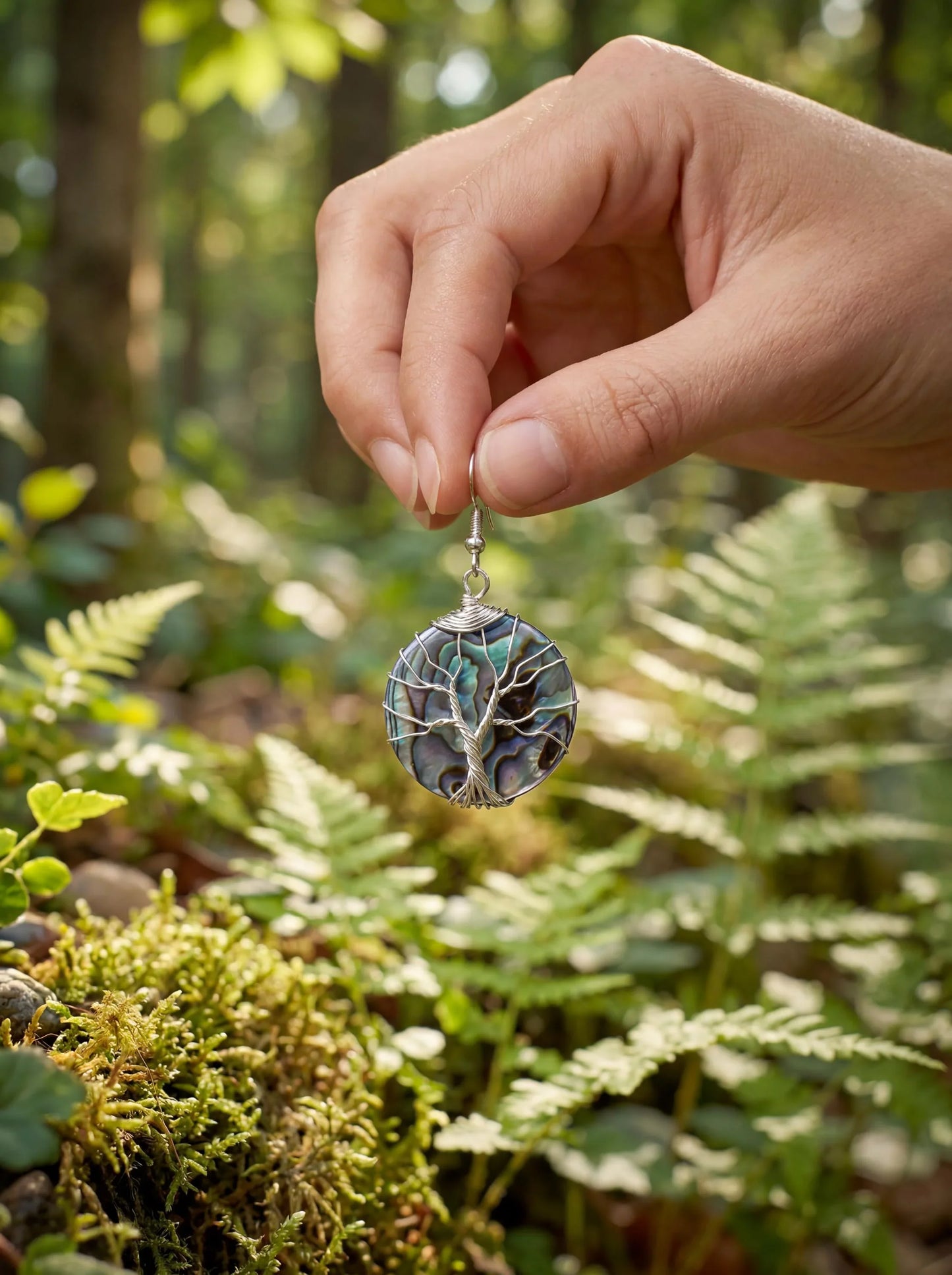 Hand holding wire-wrapped abalone pendant with tree of life design in forest setting