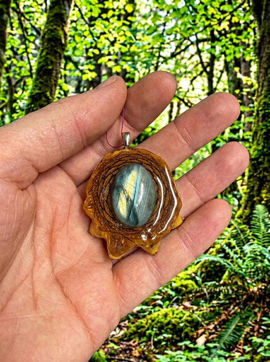 Hand holding resin pendant with labradorite stone, forest background, custom wire wrap design