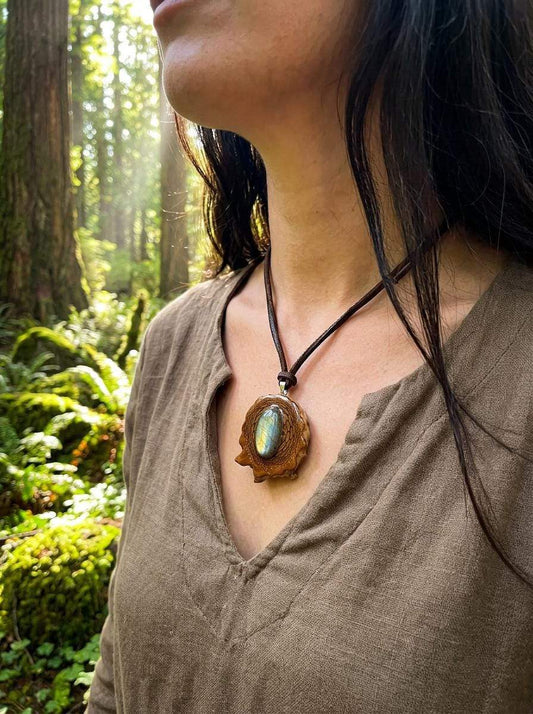 Handcrafted pinecone pendant with labradorite stone, worn on leather cord in forest setting