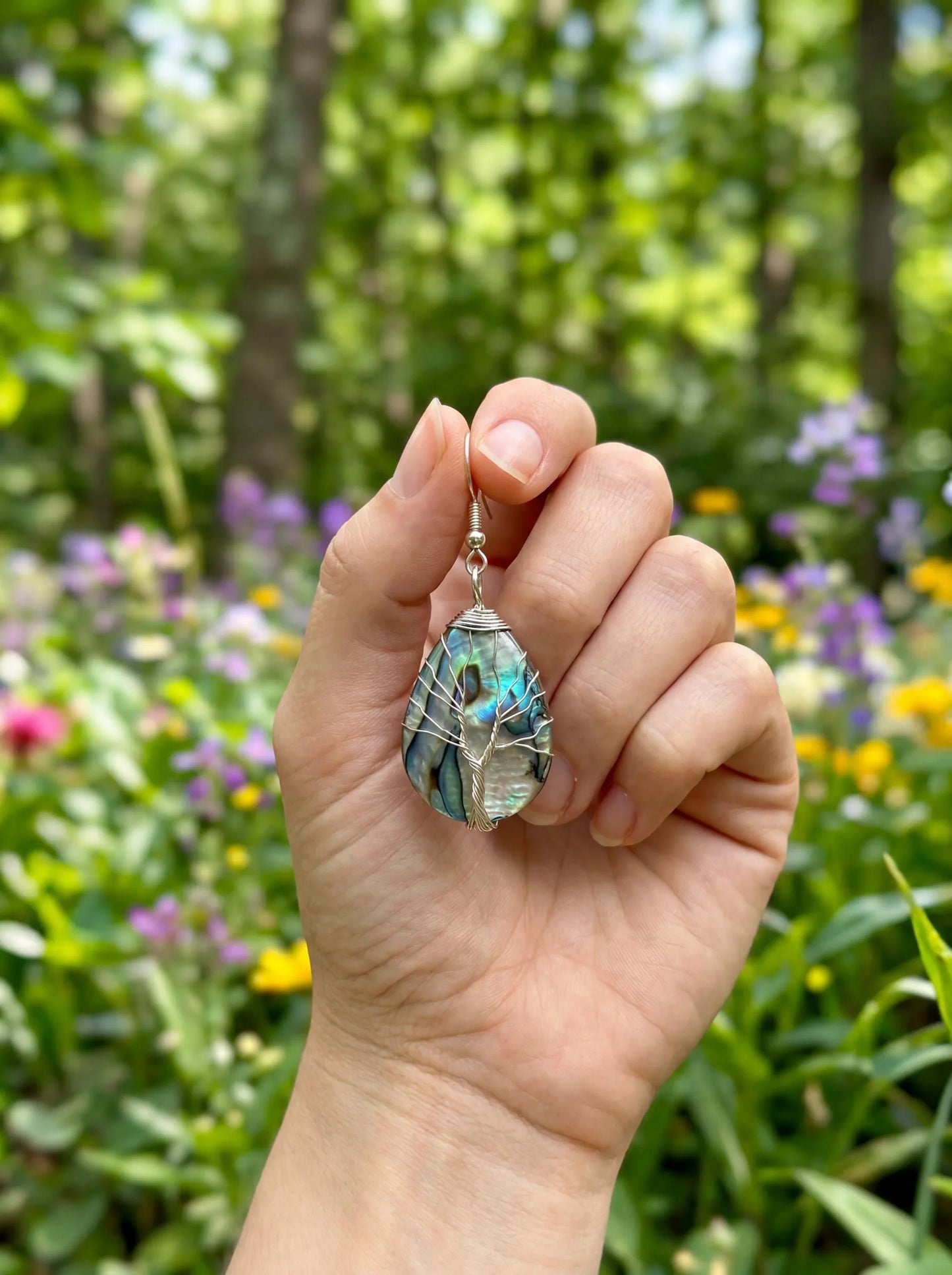 Hand holding wire-wrapped abalone shell earring with tree of life design, nature-inspired jewelry