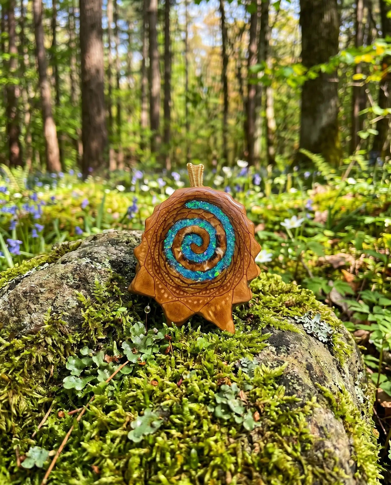 Handcrafted pinecone pendant with blue spiral resin, nestled on mossy forest rock