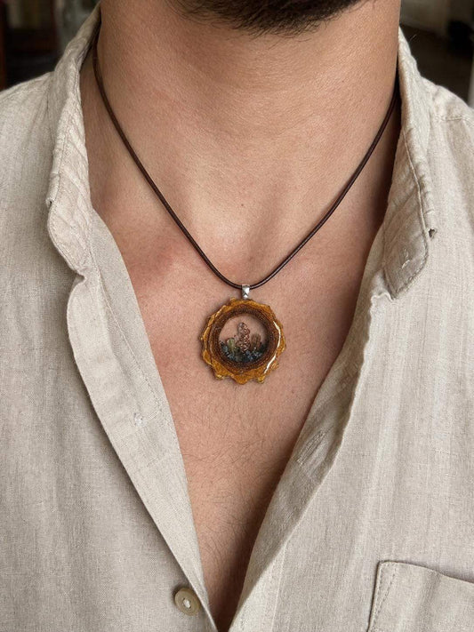 Amber resin pendant with embedded succulents and wire wrap design, worn on a leather cord.