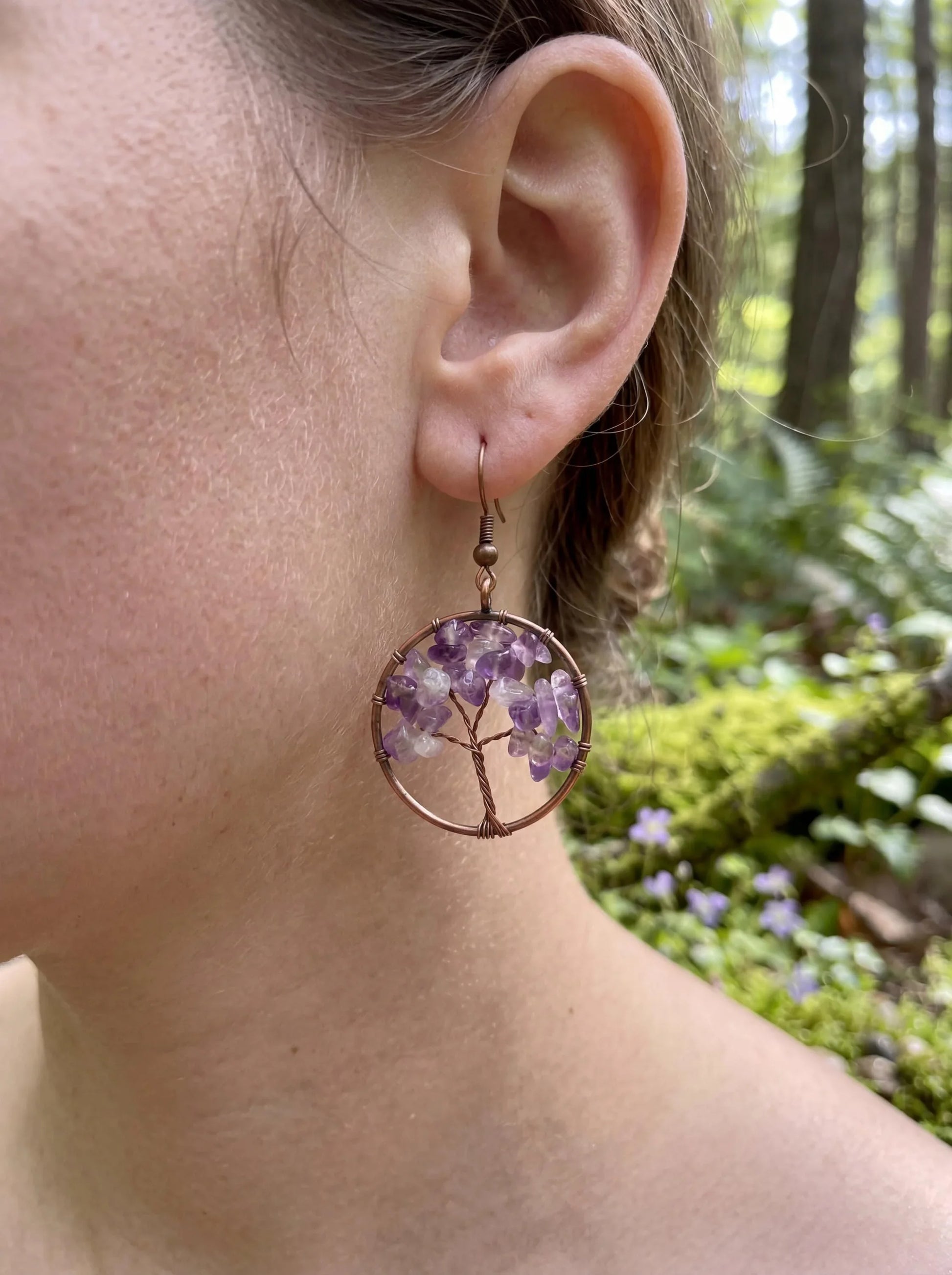Wire-wrapped amethyst tree of life earring with purple gemstones, worn in forest setting