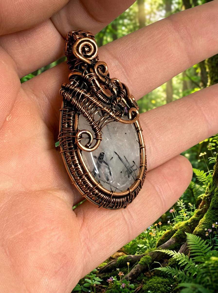 Hand holding wire-wrapped pendant with natural stone, forest background