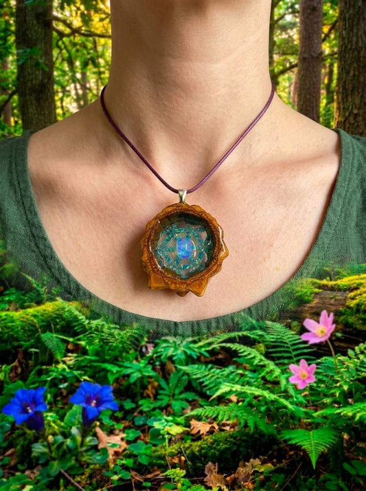 Handcrafted resin pendant with blue glitter design, worn on purple cord in forest setting