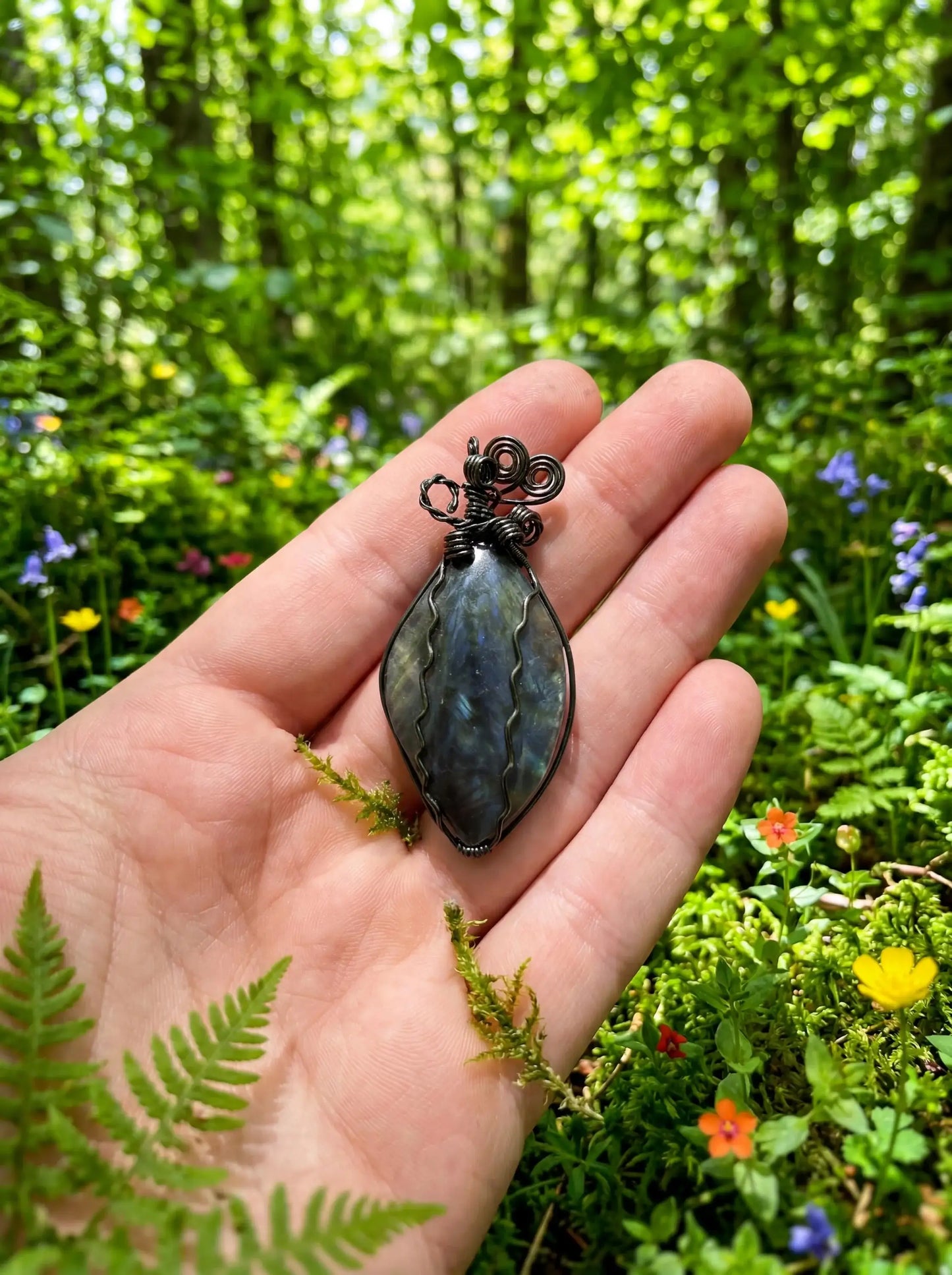 Hand holding wire-wrapped labradorite pendant in forest setting, natural stone jewelry