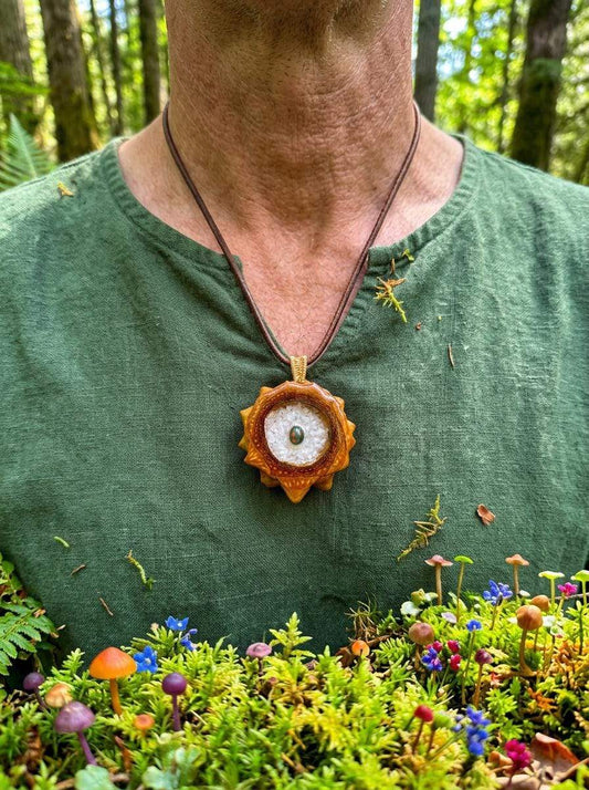 Handcrafted pinecone pendant with resin gem, worn in forest setting with moss and tiny mushrooms