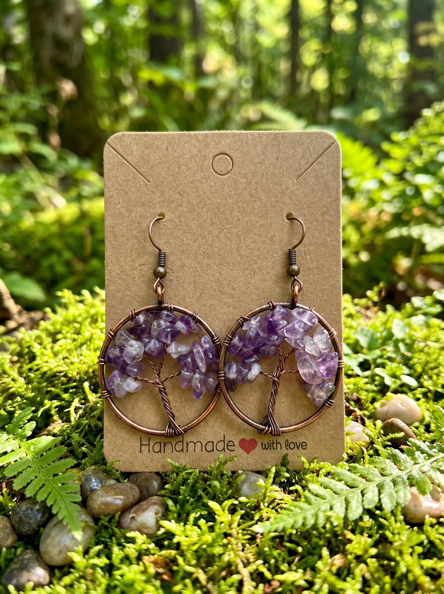 Handmade amethyst wire wrap earrings with tree of life design, displayed on card in forest setting
