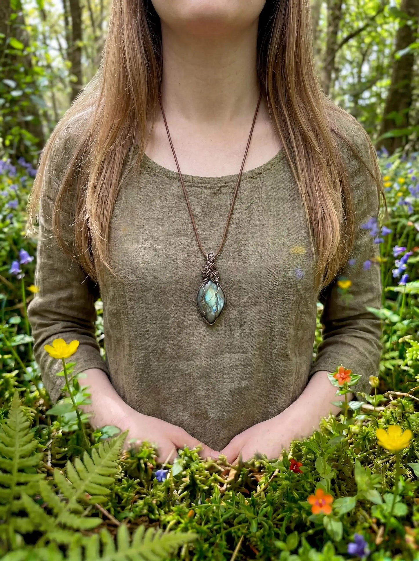 Wire-wrapped labradorite pendant necklace worn in a forest setting with wildflowers