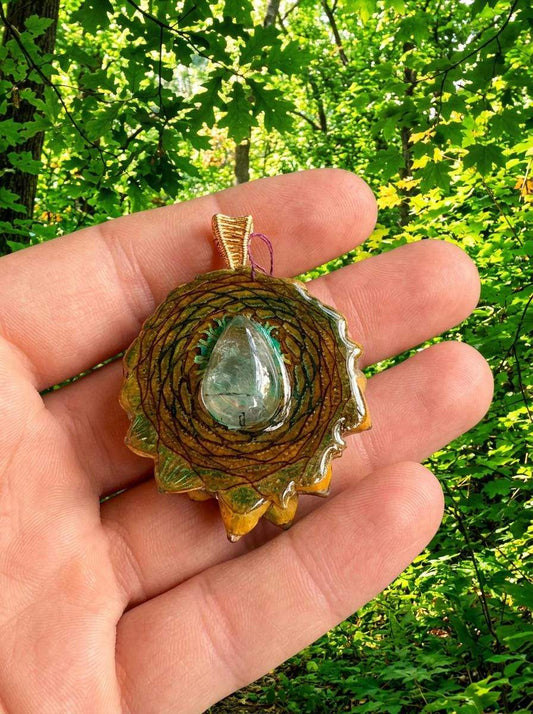 Hand holding resin pinecone pendant with crystal, wire wrap design, nature backdrop