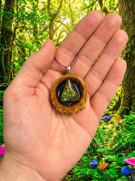 Hand holding resin pinecone pendant with glowing green triangle, forest background, custom wire wrap jewelry