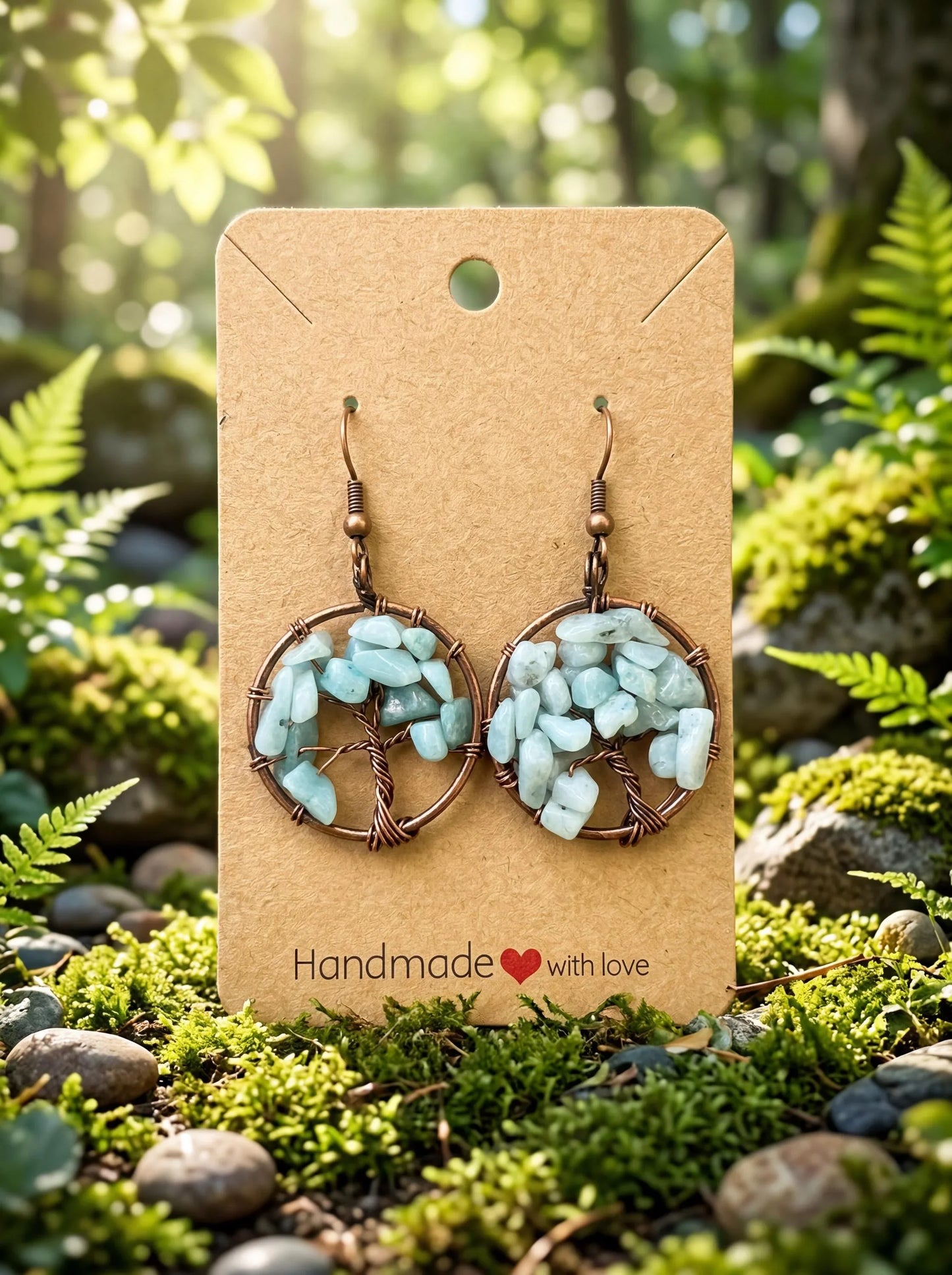 Handmade wire-wrapped earrings with light blue stone chips, displayed on a kraft card in a mossy forest setting.
