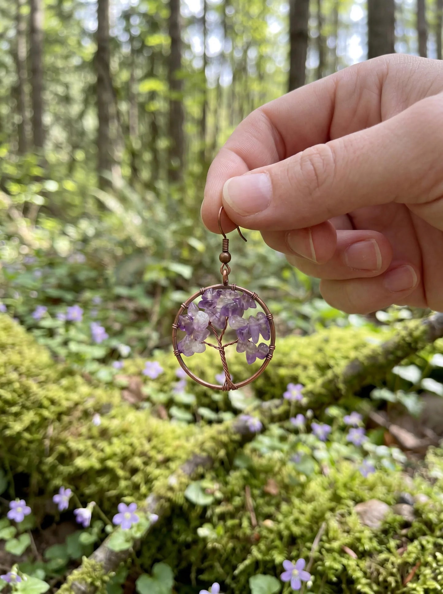 Amethyst wire-wrapped tree of life earring held in forest with moss and flowers