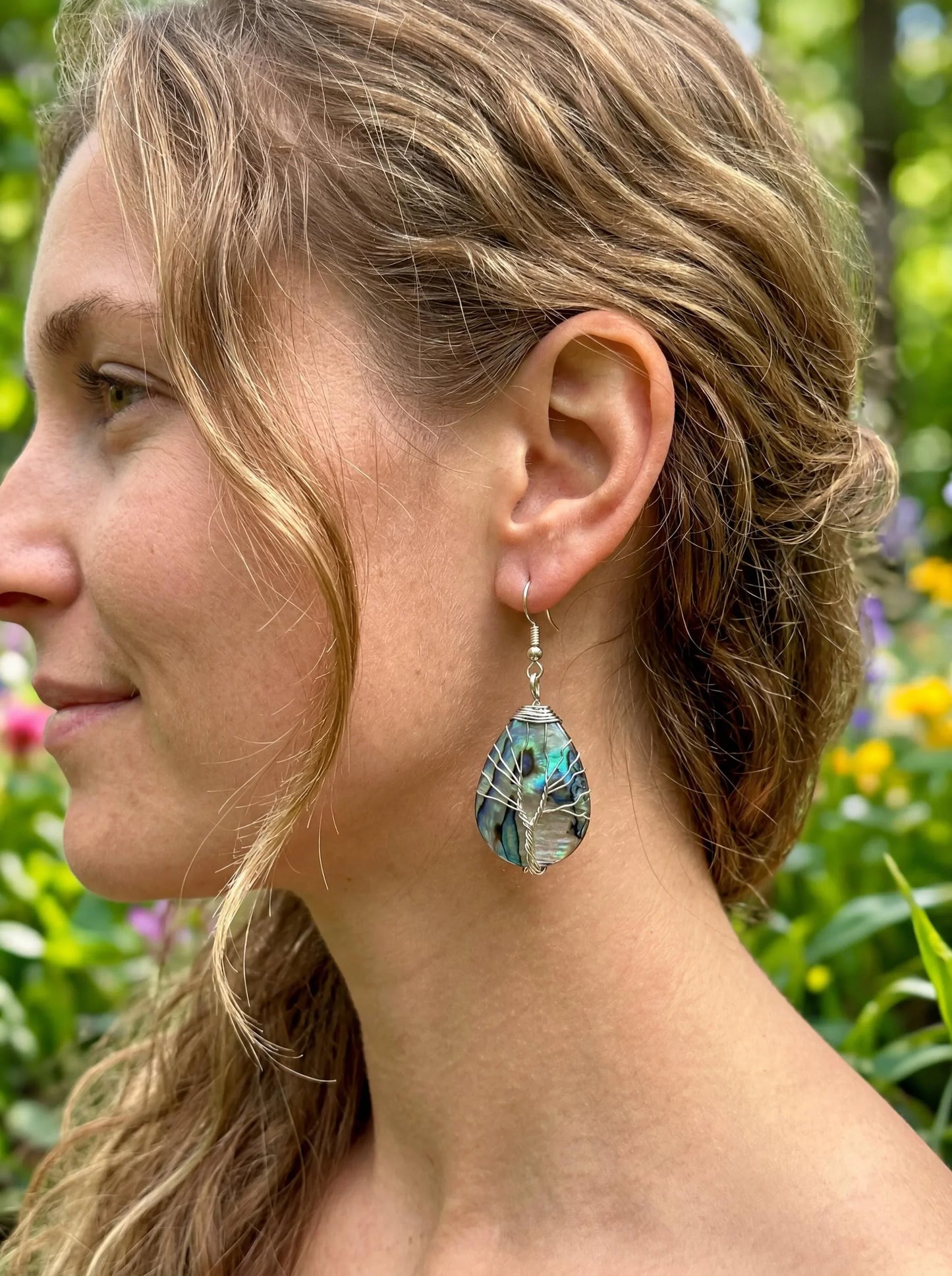 Wire-wrapped abalone shell earrings with tree of life design, worn by woman outdoors