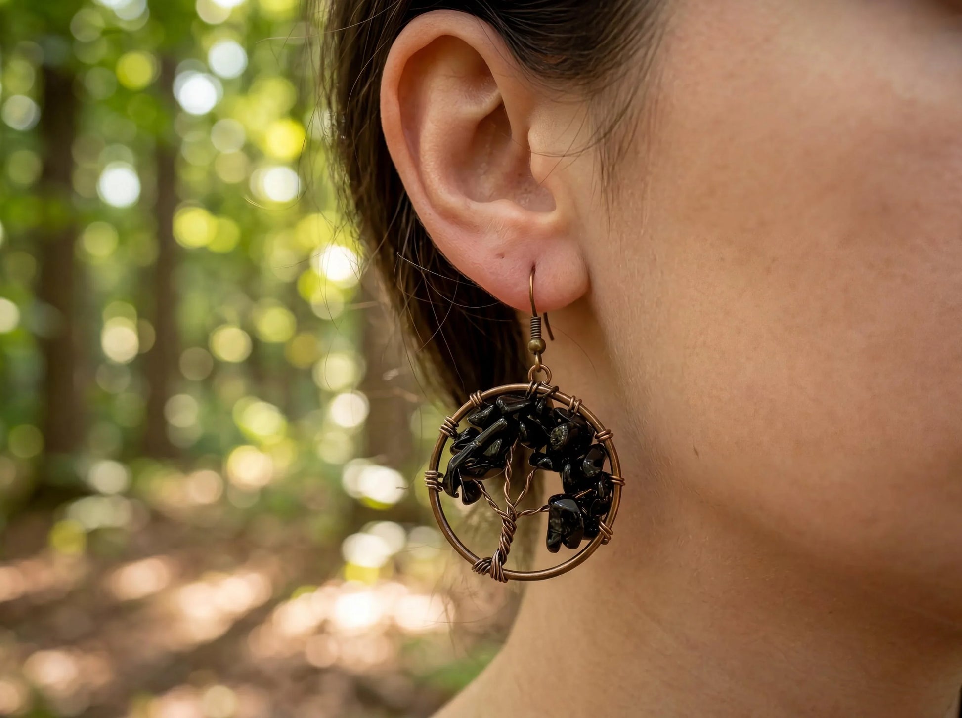 Wire-wrapped black stone earring with tree of life design, worn outdoors in forest setting