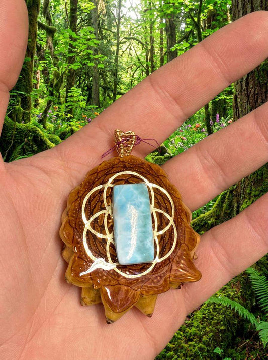 Hand holding resin pinecone pendant with larimar stone and wire wrap, forest background
