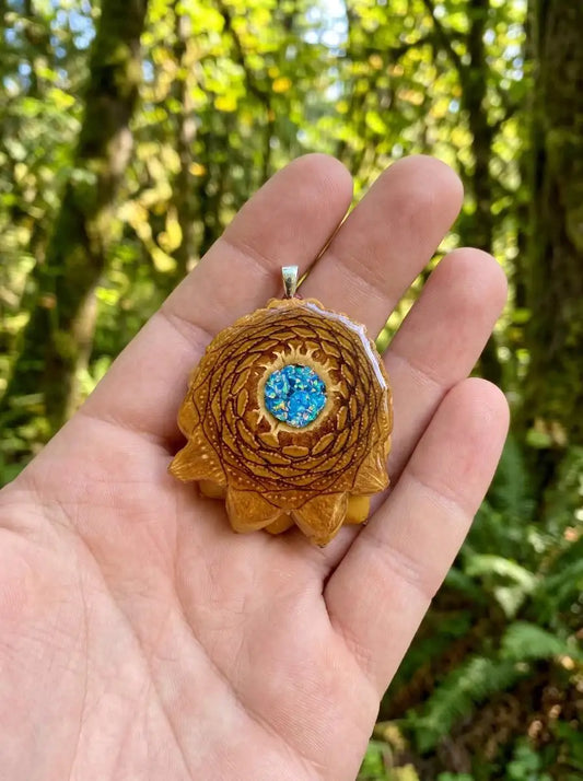 Hand holding resin pinecone pendant with blue opal center, forest background
